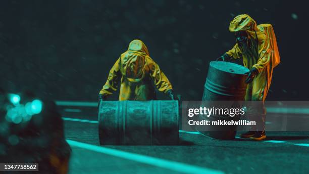 two workers with yellow protective workwear transport big barrels at night - chemical warfare stockfoto's en -beelden