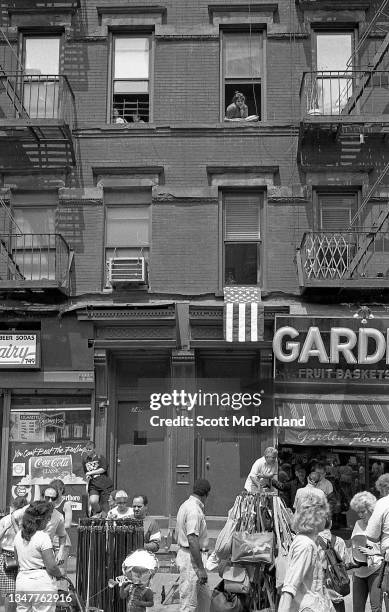 Woman looks out of a top floor window at pedestrians and vendors on the street below in Hell's Kitchen during the International Food Festival, New...