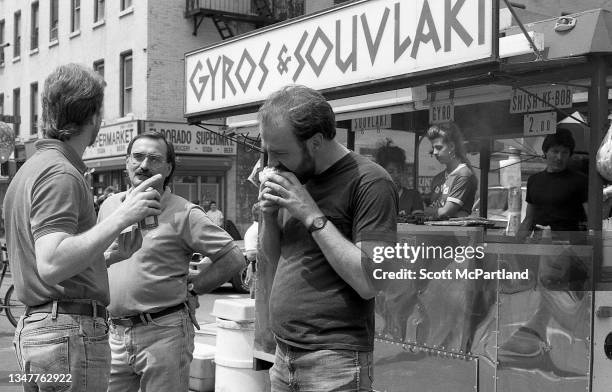 Two men talk together while a third eats a sandwich on 9th Avenue in Hell's Kitchen during the International Food Festival, New York, New York, May...