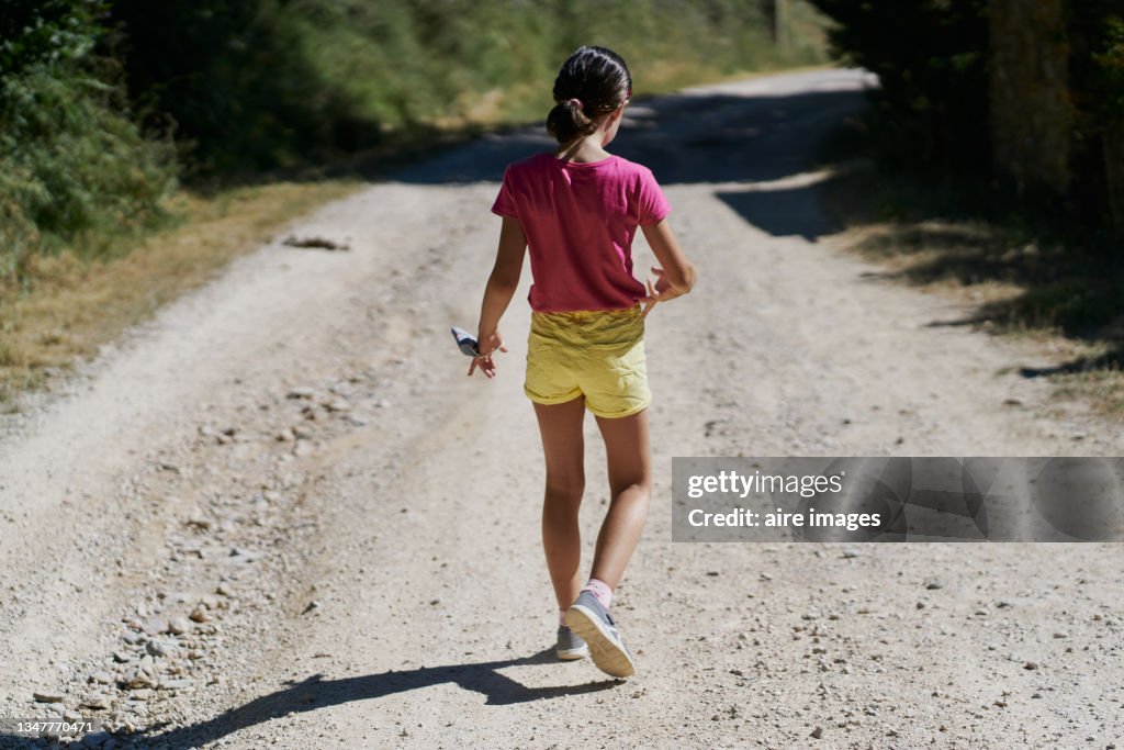 Caucasian young girl walking backwards in the middle of a field looking at the sunset