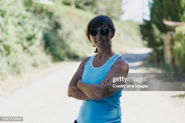 caucasian adult woman smiling crossing her arms and using black sunglasses on the road - person with arms crossed stock pictures, royalty-free photos & images