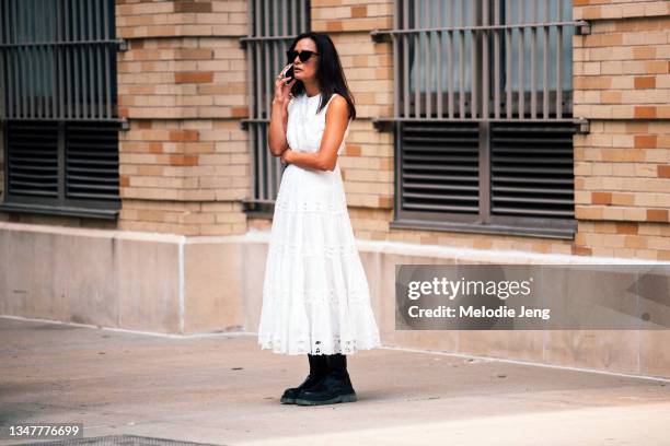 Roopal Patel talks on the phone and wears a white dress and black boots at the Rodarte show on September 11, 2021 in New York City.