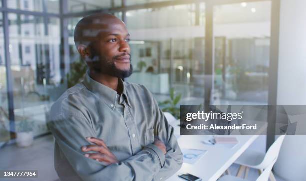 shot of a confident young businessman looking thoughtfully out of a window in a modern office - staring out window man stock pictures, royalty-free photos & images