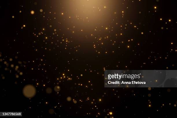 many festive golden dust on black background with warm spotlight. concept of new year or birthday celebration. perfect backdrop for your design - sparkle photos et images de collection