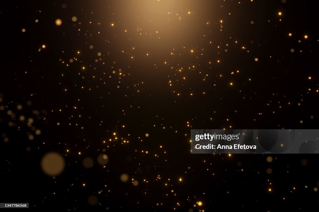 Many festive golden dust on black background with warm spotlight. Concept of New Year or birthday celebration. Perfect backdrop for your design