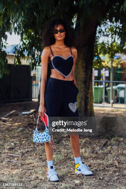 Model Cindy Bruna wears a matching Area NYC Heart cutout black top and shorts, small white and blue flora Miu Miu bag, white socks, white Nike Air...