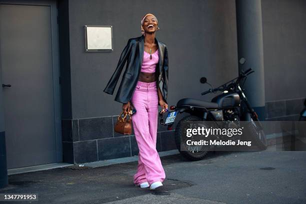 Model Mayowa Nicholas wears a headscarf, black leather jacket, matching pink crop top and pants, small Gucci brown leather bag, and white sneakers...