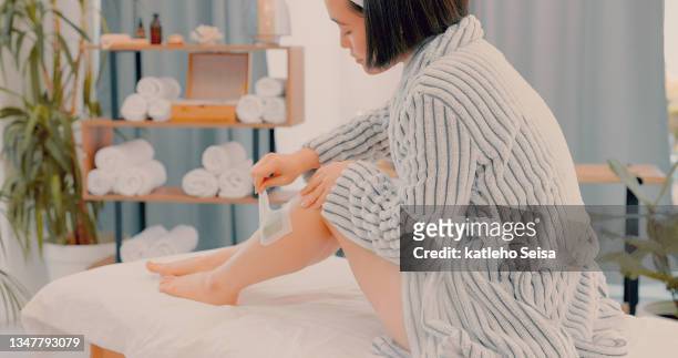 shot of an attractive young woman sitting alone on a bed in the spa and waxing her legs - wax figure stockfoto's en -beelden