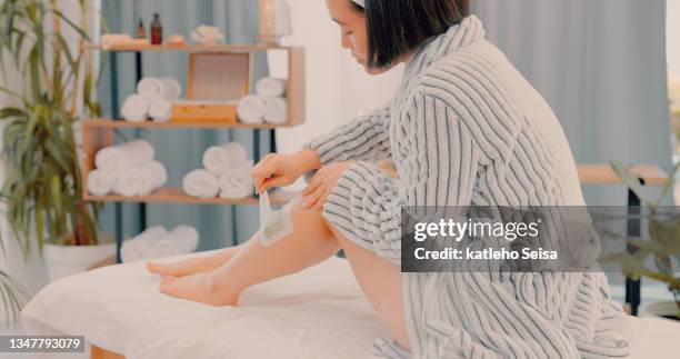 shot of an attractive young woman sitting alone on a bed in the spa and waxing her legs - wax figure stock pictures, royalty-free photos & images