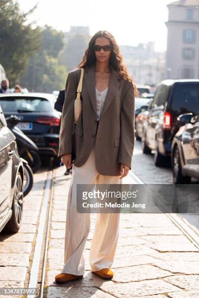 Model Jordan Daniels wears an oversized gray blazer, white vest, yellow purse, cream pants, and brown suede Birkenstock clogs after the Tod's show...