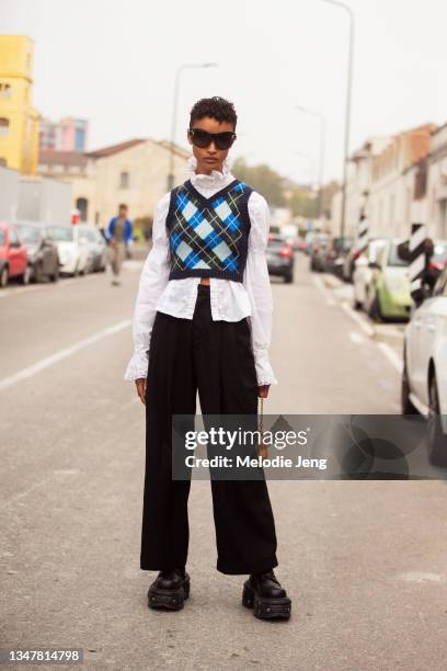 Model Georgia Palmer wears oversized sunglasses, a plaid cropped knit vest over a white shirt, black wide-legged trousers, and chunky black boots...