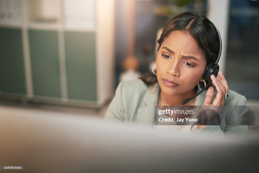 Shot of a young woman using a headset and looking stressed in a modern office
