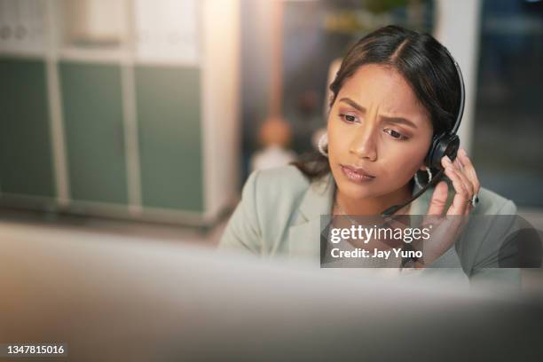 tiro de uma jovem usando um fone de ouvido e olhando estressado em um escritório moderno - sem esperança - fotografias e filmes do acervo