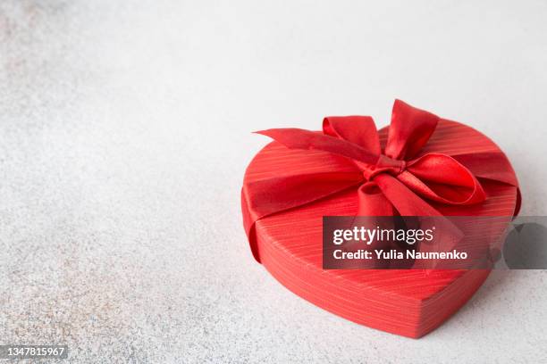 red gift box with bow in the form of heart on a light background. - gift box tag stock-fotos und bilder