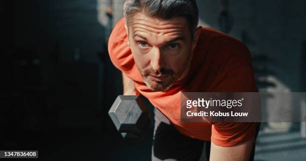 shot of a handsome mature man using dumbbells during his workout in the gym - determination face stock pictures, royalty-free photos & images