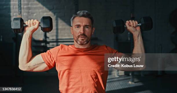 shot of a handsome mature man sitting alone and using dumbbells for shoulder press exercises in the gym - dumbbell stock pictures, royalty-free photos & images