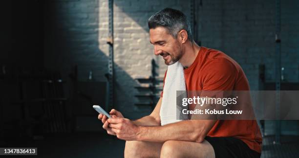 shot of a handsome mature man sitting alone in the gym and using his cellphone after his workout - after workout towel happy stock pictures, royalty-free photos & images