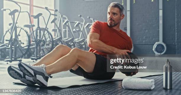 colpo di un bell'uomo maturo che usa una palla medica durante il suo allenamento in palestra - adults working out foto e immagini stock