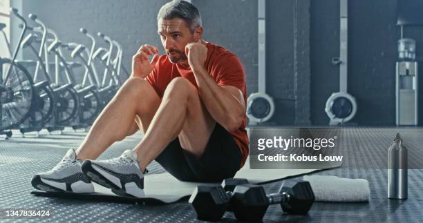 shot of a handsome mature man doing sit-ups while working out in the gym alone - sit ups stockfoto's en -beelden