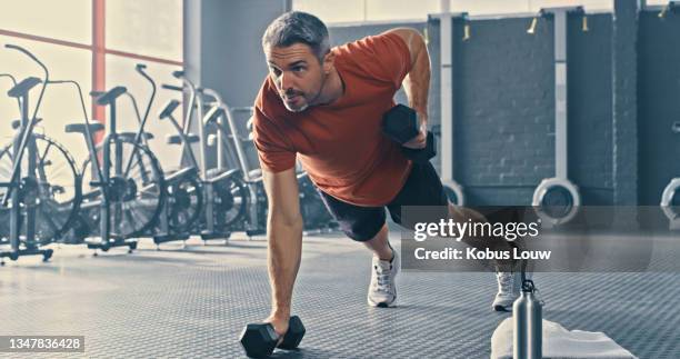 foto de un apuesto hombre maduro usando mancuernas durante su entrenamiento en el gimnasio - entrenamiento de fuerza fotografías e imágenes de stock