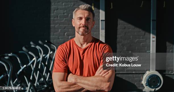 shot of a handsome mature man standing with his arms folded after his workout in the gym - athlete training stockfoto's en -beelden