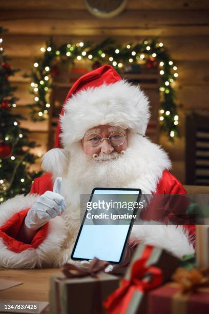 smiling santa claus shows a  digital tablet with white chroma key on a screen, looking into camera - chat noel stockfoto's en -beelden