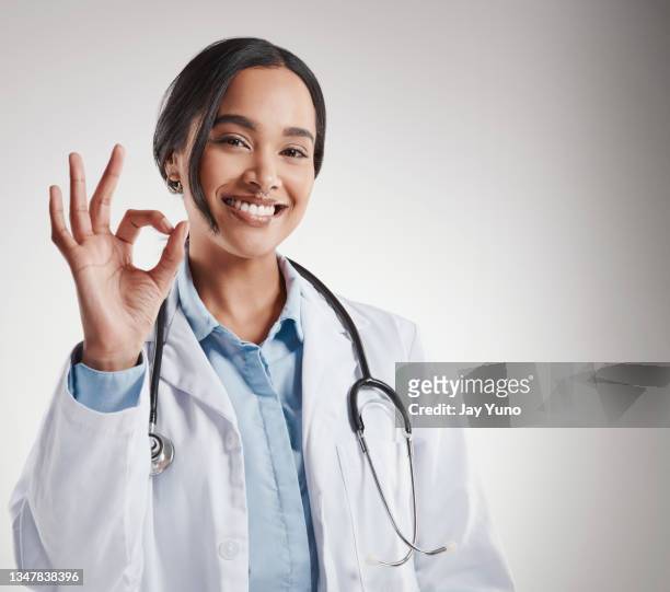 shot of a female doctor showing the ok sign while standing against a grey background - jay luck stock pictures, royalty-free photos & images