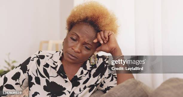 shot of a mature woman being stressed on the couch at home - mourner stockfoto's en -beelden