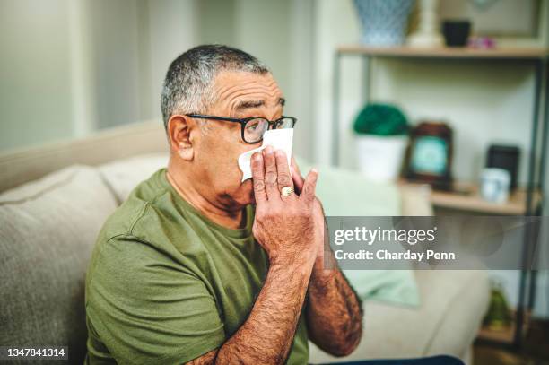 shot of a senior man blowing his nose with a tissue at home - hispanic person sick 個照片及圖片檔