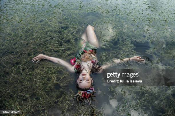 woman in dress with flowers lying in water of lake - women in see through dresses stock-fotos und bilder