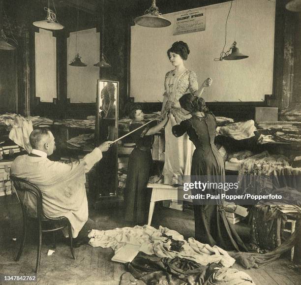 Les Createurs de la Mode image of a model having a dress fitted to her in a Parisian workroom, an apprentice designer sits in a chair and points to a...