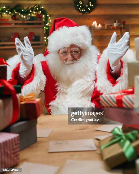 eine nahaufnahme des weihnachtsmanns, der in eine kamera schaut und an einem tisch im weihnachtsinneren sitzt - santa close up stock-fotos und bilder