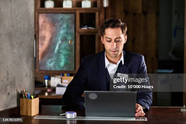 male hotel receptionist looking at laptop on desk - name tag fotografías e imágenes de stock