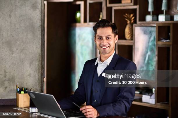 portrait of cheerful hotel receptionist smiling towards camera - reception hotel stock pictures, royalty-free photos & images