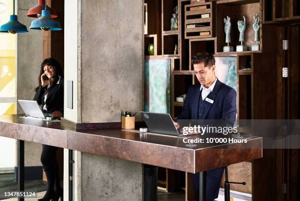 two hotel receptionists working on front desk - booking hotel foto e immagini stock