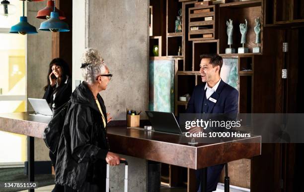 cheerful male receptionist serving woman in hotel - check in airport stock-fotos und bilder