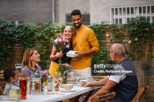 happy young man with bouquet and gift hugging his senior mother in law outdoors in garden. - mother day stockfoto's en -beelden