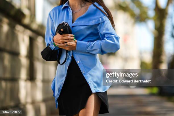 Guest wears a blue shiny satin shirt, a black nylon clutch from Prada, a black slit / split short skirt, rings, a silver chain necklace, outside Rick...