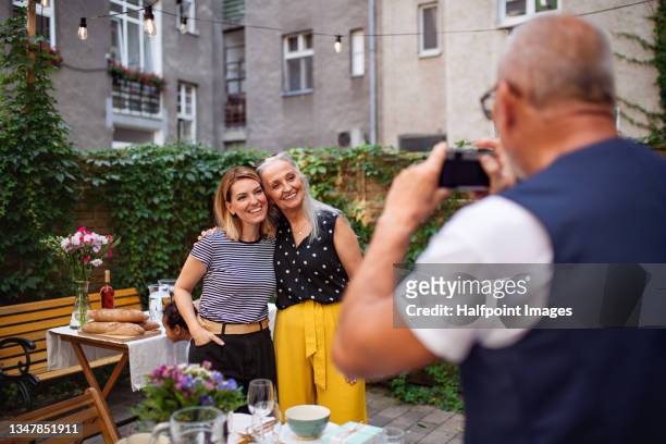 senior man taking photograph of his wife and daughter outdoors in front or back yard. - old photographer stock-fotos und bilder