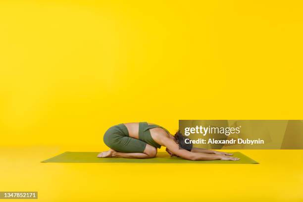 woman doing yoga on mat in child pose on floor on yellow background relaxing. sport concept and healthy lifestyle - mat stock-fotos und bilder