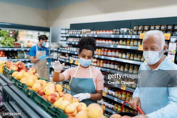american employee in supermarket assisting senior customer while buying fruits and vegetables - supermarket mask stock pictures, royalty-free photos & images