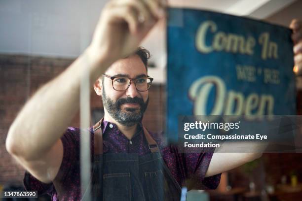 business owner setting up open sign in cafe window - wiedereröffnung stock-fotos und bilder