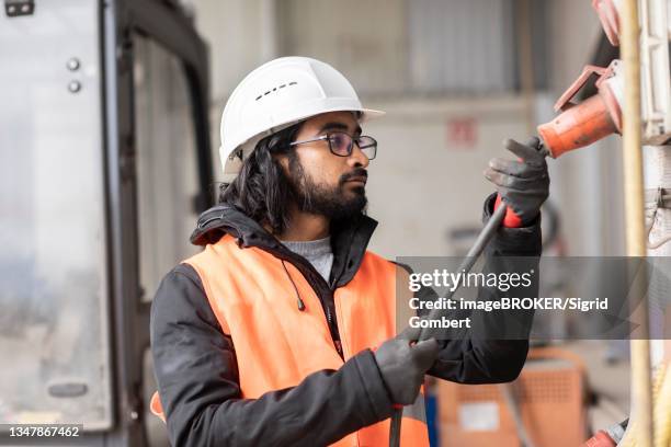 technician with beard and helmet works in a workshop, freiburg, baden-wuerttemberg, germany - migrant worker stock-fotos und bilder