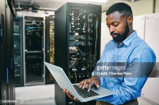 foto de un joven usando una computadora portátil mientras trabajaba en una sala de servidores - information technology support fotografías e imágenes de stock
