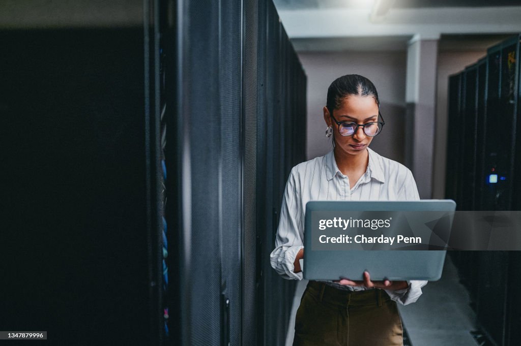 Aufnahme einer jungen Frau mit einem Laptop bei der Arbeit in einem Serverraum