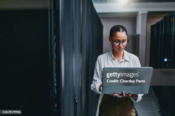 tiro de uma jovem usando um laptop enquanto trabalhava em uma sala de servidor - computer science - fotografias e filmes do acervo