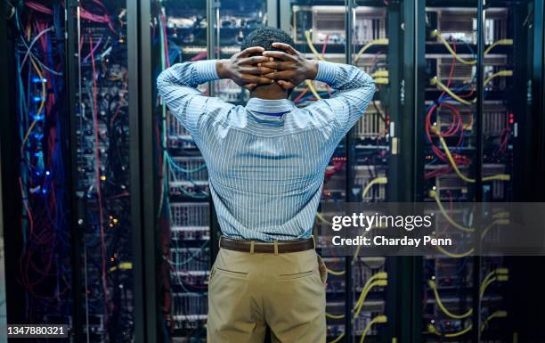 rearview shot of a young man standing with his hands behind his head while struggling with a technical issue in a server room - glitch technique stockfoto's en -beelden