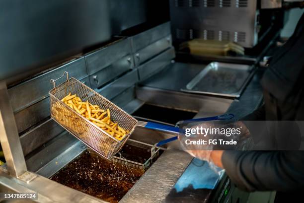 weibliche hände, die eine bratpfanne mit pommes frites in einer großküche halten - fast food french fries stock-fotos und bilder