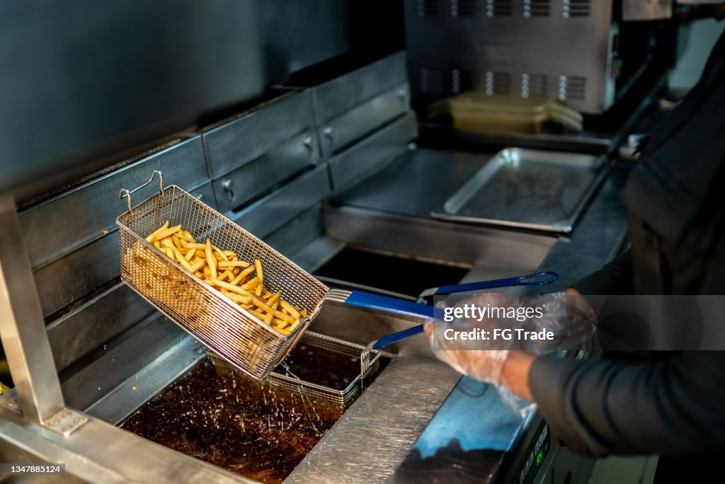 Mãos femininas segurando uma frigideira com batatas fritas em uma cozinha comercial