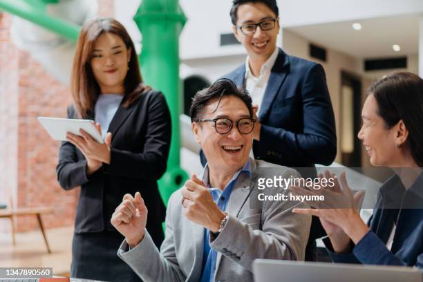 excited asian business team celebrating success in office - business people cheering in office stockfoto's en -beelden